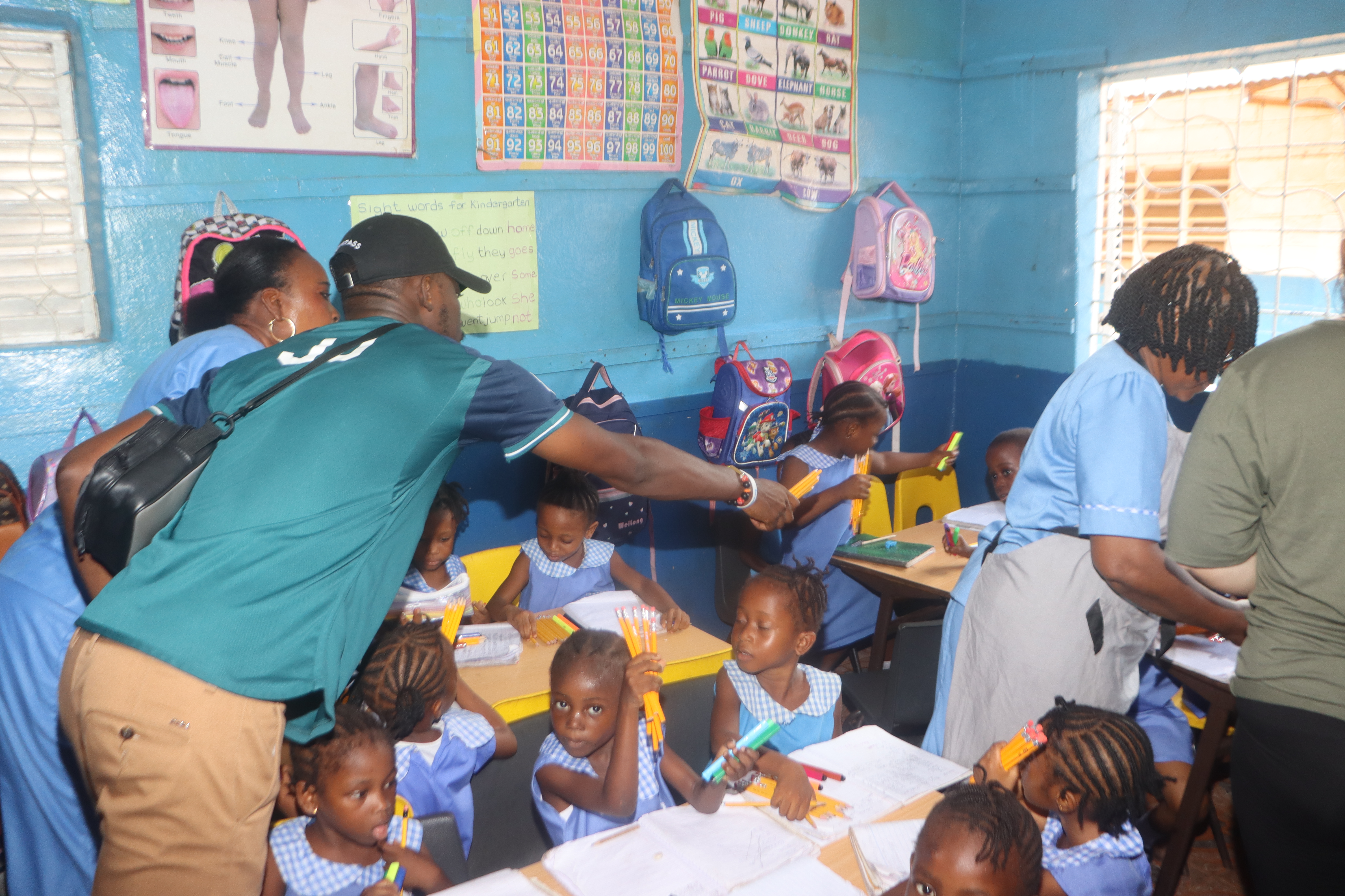 Joseph - a Develop Africa Sierra Leone staff - and teachers distributing coloring pens and pencils to kids in a classroom in Sierra Leone