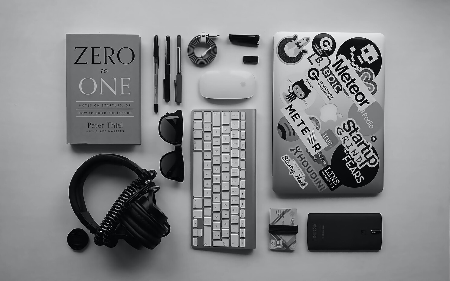 (c) Unsplash. A book, headset, pens, pencils, keyboard, mouse, laptop, and other mobile device accessories on a table.