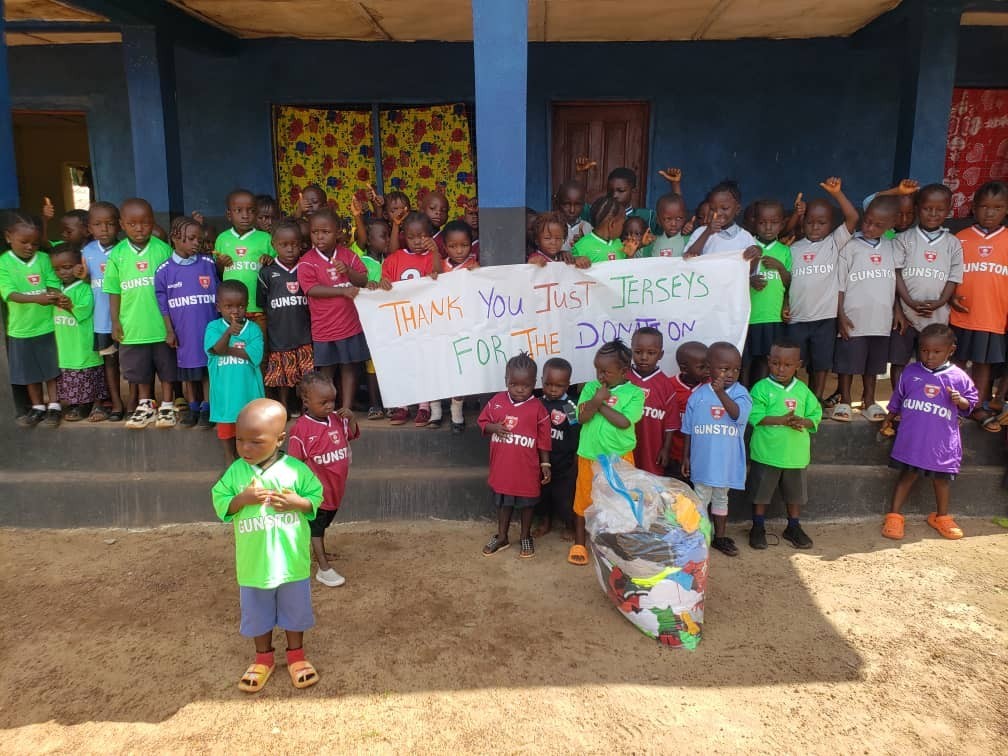 (c0 Develop Africa. Kids in Kamawornie with jersey and banner thanking Develop Africa for the jersey.
